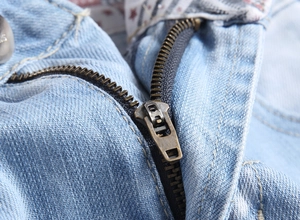 Detailaufnahme von Messingreißverschluss und weißer Naht auf hellblauen Denim-Shorts