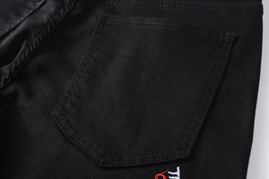 Détail de la poche arrière du jean slim noir avec broderie de lettres TR rouges et blanches