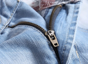 Detailed close-up of high-quality copper metal zipper on light blue denim shorts