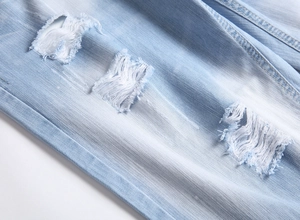 Makroaufnahme von hellblauem Denim-Stoff mit Distressed-Löchern und Fransen-Details