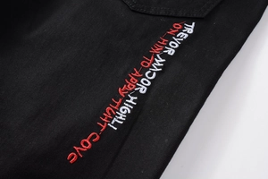 Gros plan sur la broderie rouge et blanche sur le tissu en denim noir extensible