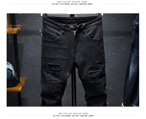 Detail of black slim fit jeans with stylish ripped holes and patch texture design