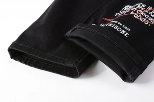 Détail du jean slim noir de style urbain avec imprimé graphique blanc et rouge sur le bas