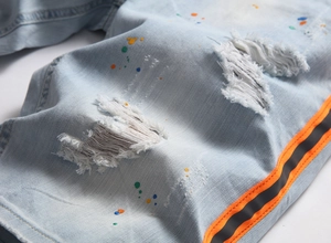 Dettaglio di jeans azzurri con macchie di vernice colorate e fettuccia laterale in tessuto