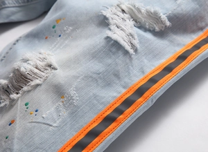 Dettaglio macro dei jeans azzurri strappati con schizzi di colore e nastro laterale a righe