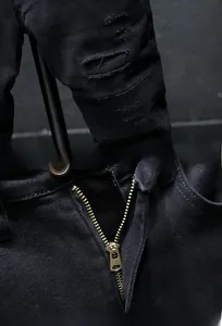 Detailed close-up of heavy denim texture with distressed knee holes and metal zipper fly