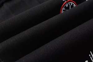 Détail de la broderie horloge rouge et texte blanc sur tissu denim extensible noir