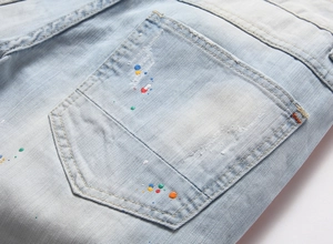 Dettaglio della tasca in denim azzurro con schizzi di vernice colorata e strappi vintage
