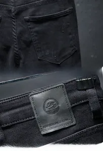 Detail of men's black distressed denim jeans featuring back pocket rips and leather waist tag