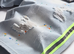 Détail d'un short en jean bleu clair avec éclaboussures colorées et bande réfléchissante