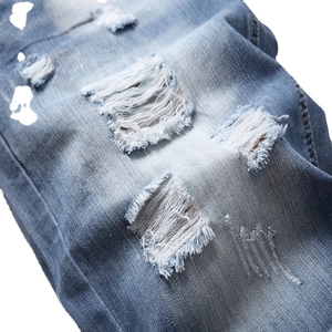 Men's light blue distressed denim shorts with heavy ripped details and street style whiskers