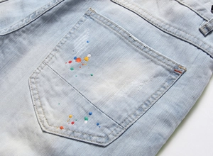 Détail d'un jean bleu clair avec des éclaboussures de peinture colorées sur la poche