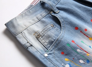 Détail de short en jean bleu clair avec éclaboussures de peinture colorées et rivets en métal