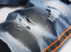 Detail of distressed light blue denim shorts with colorful paint splashes and side webbing