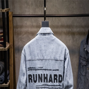 Detail of light blue denim jacket back with RUNHARD lettering on industrial wall