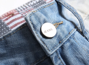Détail de la taille du jean avec bouton JEANS argenté et doublure à carreaux