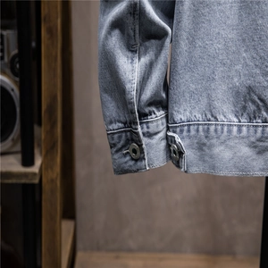 Detail view of light blue washed denim jacket fabric with stitching and metal button