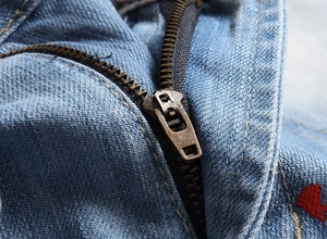 Détail d'une fermeture éclair en cuivre et de coutures jaunes sur un short en denim bleu