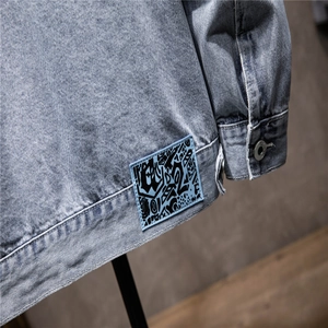 Detail of light blue denim jacket showing art patch and silver button cuff close-up