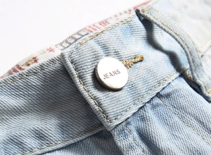 Détail du bouton en métal argenté et des surpiqûres dorées sur le jean en denim