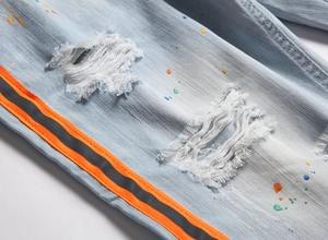 Dettaglio di jeans azzurri con macchie di vernice e striscia laterale riflettente