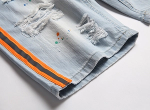 Dettaglio dei jeans azzurri con macchie di vernice, fori usurati e nastro a righe arancioni