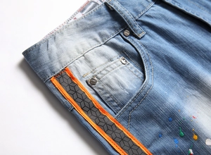 Detail of light blue denim shorts with colorful paint splatters and side webbing