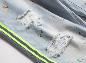 Détail d'un jean bleu clair délavé avec des taches de peinture et des déchirures stylées