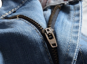 Detail of the high-quality bronze metal zipper and yellow stitching on blue denim shorts
