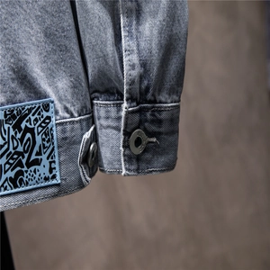 Close-up of denim jacket cuff with metal buttons and street-style graphic patch