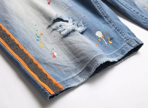 Detail of light blue denim shorts with colorful paint splatters and side striped webbing