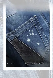 Macro detail of blue denim shorts showing paint splatter texture and black pocket stitching