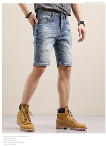 Détail du short en jean bleu avec taches de peinture colorées et effet moustaches usé