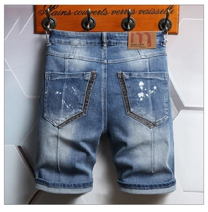 Detailed view of men's blue denim shorts with white paint splatter on the back pocket