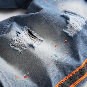 Distressed blue denim shorts with colorful paint splatters and reflective orange webbing