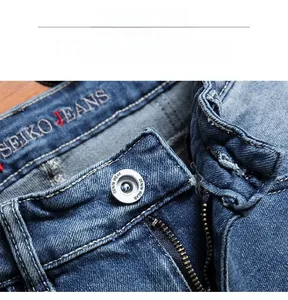Macro detail of dark blue denim waist featuring branded button and brass zipper