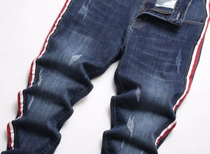 Détail de jean bleu foncé avec rayures latérales rouge-blanc-noir et texture vieillie