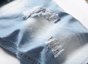 Detailed close-up of light blue denim shorts featuring distressed rips and frayed edges