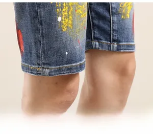 Detailed close-up of dark blue denim shorts with artistic yellow and red paint splatters