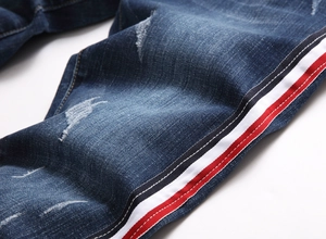 Gros plan sur un jean bleu usé avec des bandes latérales rouges et blanches brodées
