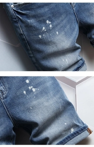 Detail of light blue distressed denim shorts with white ink splatter and folded hem