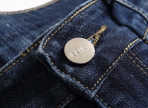 Vue macro d'un bouton métallique argenté avec gravure JEANS et coutures jaunes sur denim