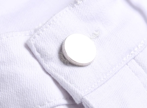 Close-up of polished silver metal button on white stretch denim fabric with fine stitching