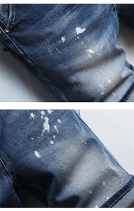 Detail of blue denim shorts showing white paint splatter and distressed wash texture