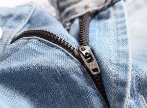 Detailed macro view of vintage bronze metal zipper on light blue washed denim shorts