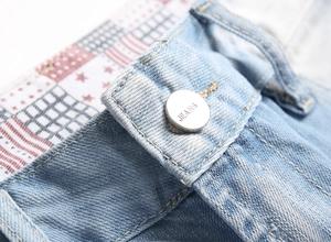 Close-up of metal button and patterned waistband lining on light blue denim shorts