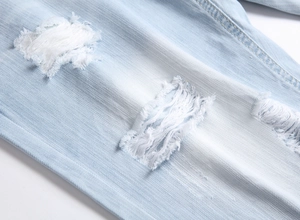 Close-up detail of light blue denim shorts with distressed holes and frayed edges texture