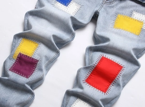Detail of light blue washed jeans featuring colorful embroidered patches and retro stitching