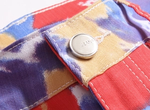 Makro-Detail des silbernen Metallknopfes an der bunten Batik-Stretch-Denim-Jeans für Herren