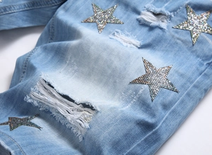 Detail of light blue denim fabric with distressed holes and sparkling star embroidery patches